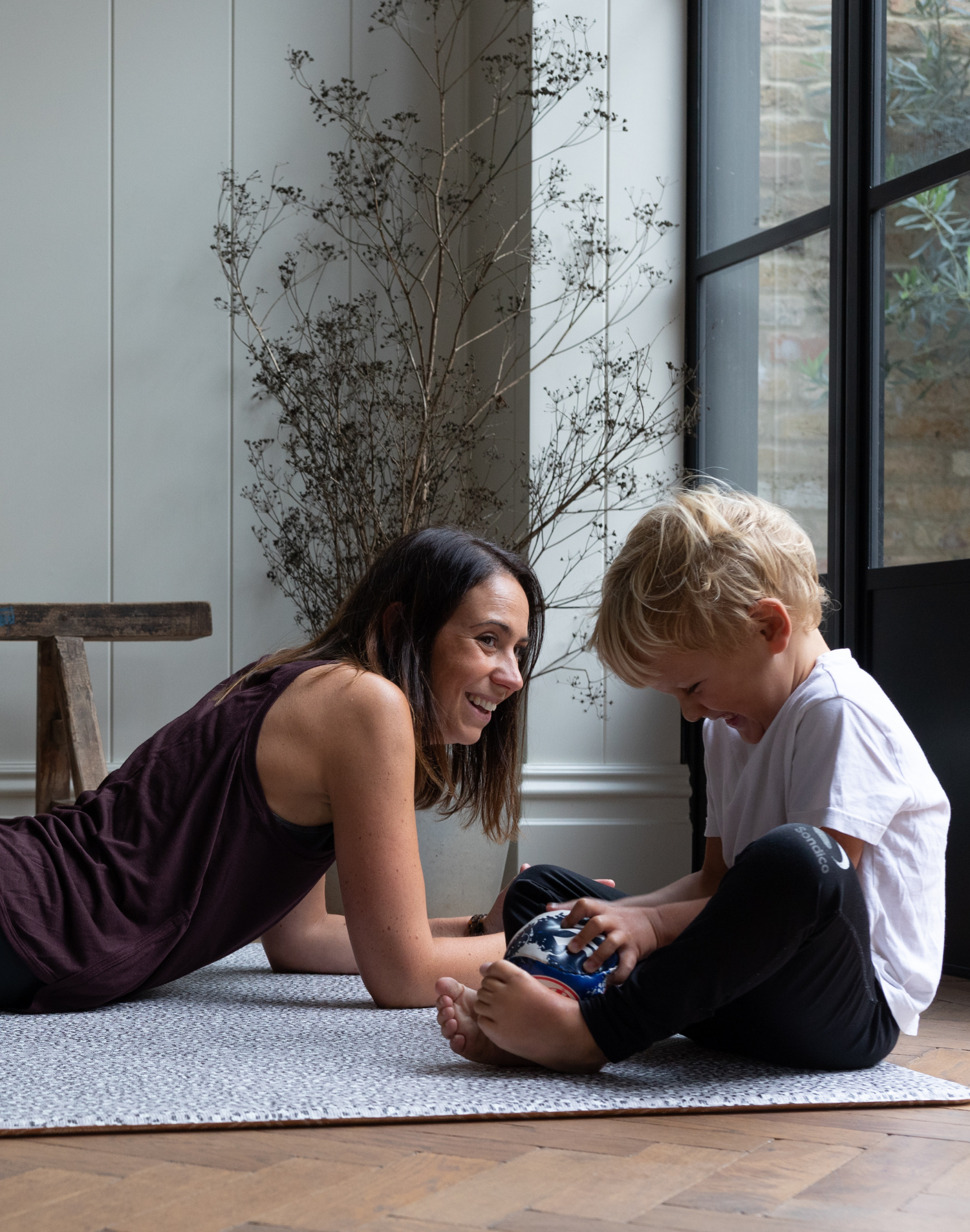 Exercising lady and boy giggle on the floor supported by leopard print playmat by totter and tumble 