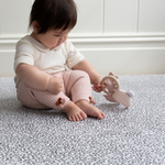 Sitting baby plays with teething toy on supportive and soft sufrace of grey leopard print playmat