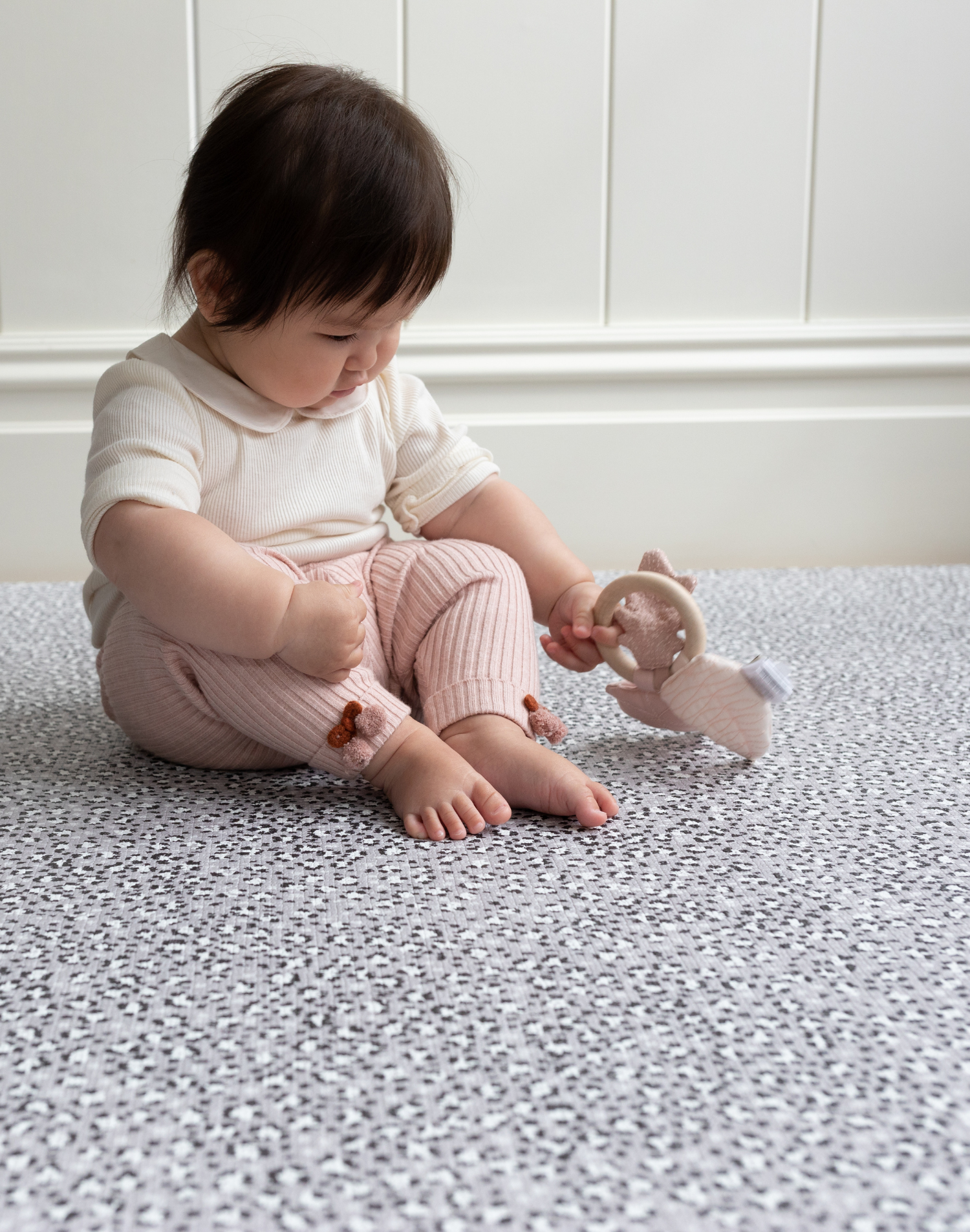 Sitting baby plays with teething toy on supportive and soft sufrace of grey leopard print playmat