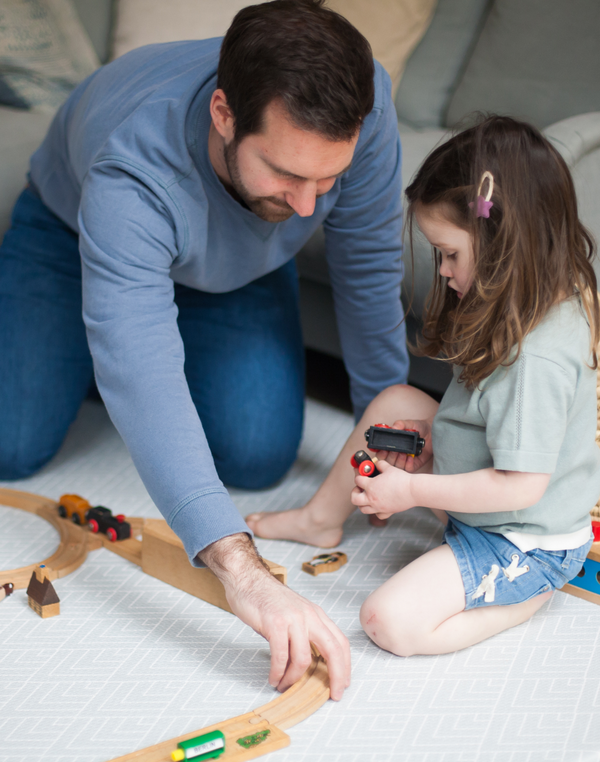 Father and daughter play together on foam grey playmat designed to look like a rug in the home while providing support 