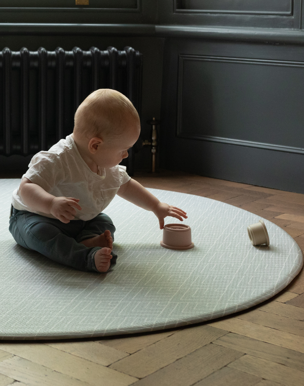 Little boy enjoys stacking cups on large round baby playmat with plenty of space to play
