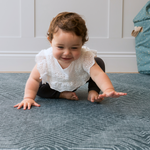 Toddler sitting on teal Wanderlust play rug by Totter and tumble with thick foam to support floor play for the whole family 