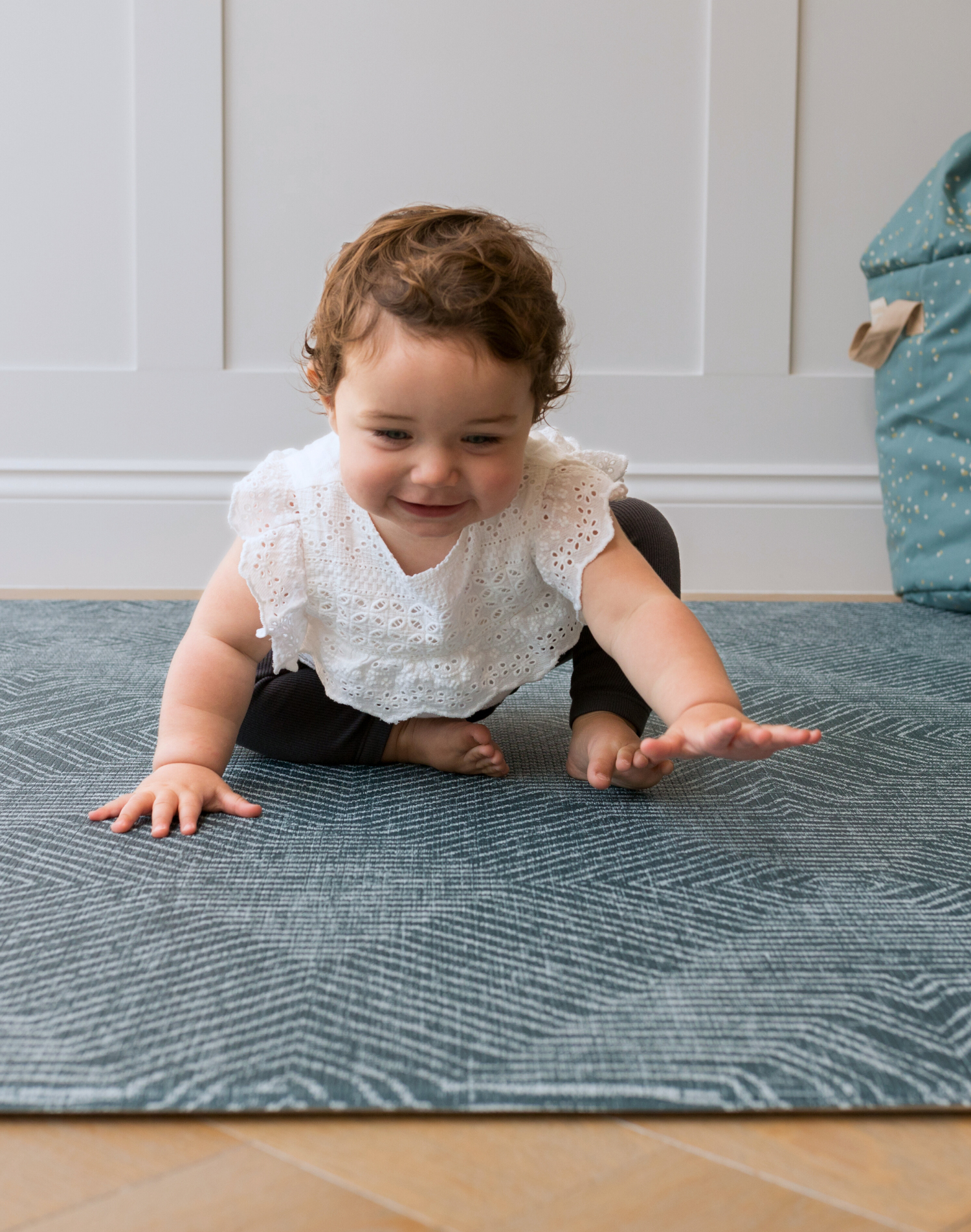 Toddler sitting on teal Wanderlust play rug by Totter and tumble with thick foam to support floor play for the whole family 