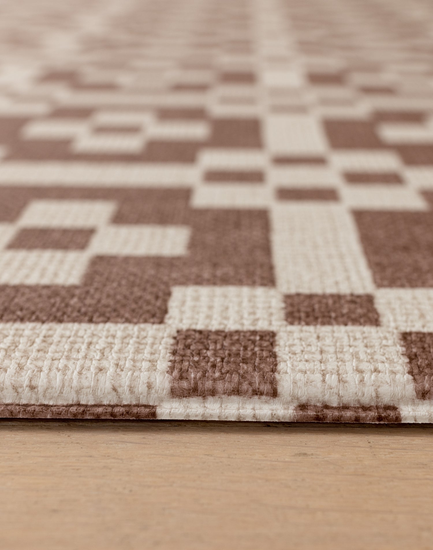Close up of a 1.3cm thick crawling mat for newborns+. The playmat features a Portcullis motif in roasted umber + birch.