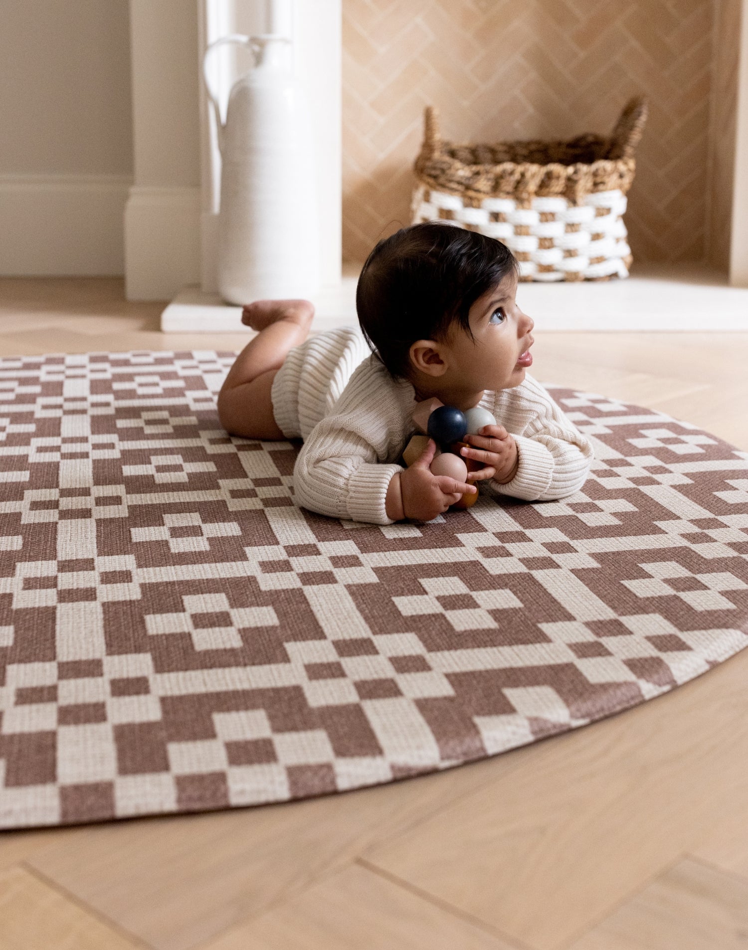 A baby crawls on a round brown patterned playmat. The room has stylish neutral tones