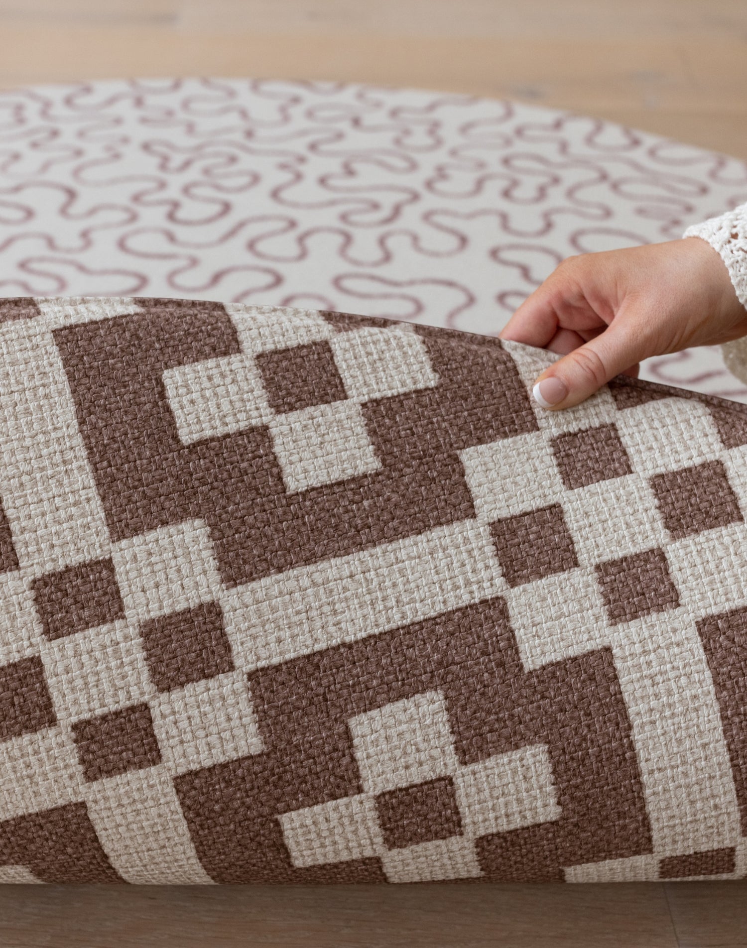 A hand folds over a Totter + Tumble reversible baby mat, revealing  a hexagon play mat design in brown on the reverse.