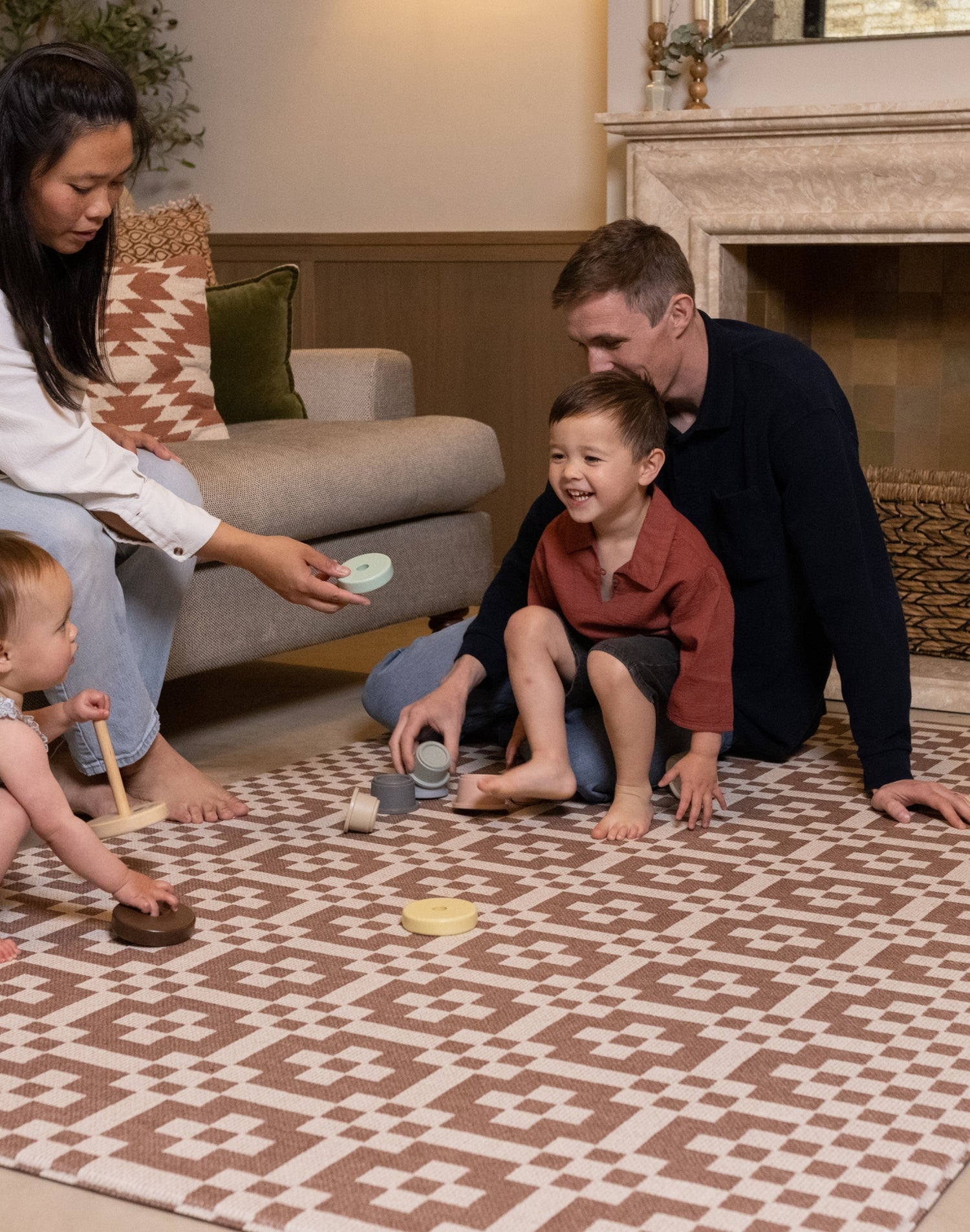 Family playing with toys on an extra large playmat for toddlers in a chic neutral living room.