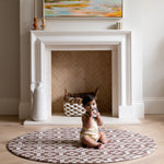 Child sitting on a checkered round baby play mat in a room with a fireplace and painting.