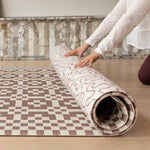 Hands gently roll out a reversible Totter + Tumble play mat for baby. The playmat shows a n earthy motif