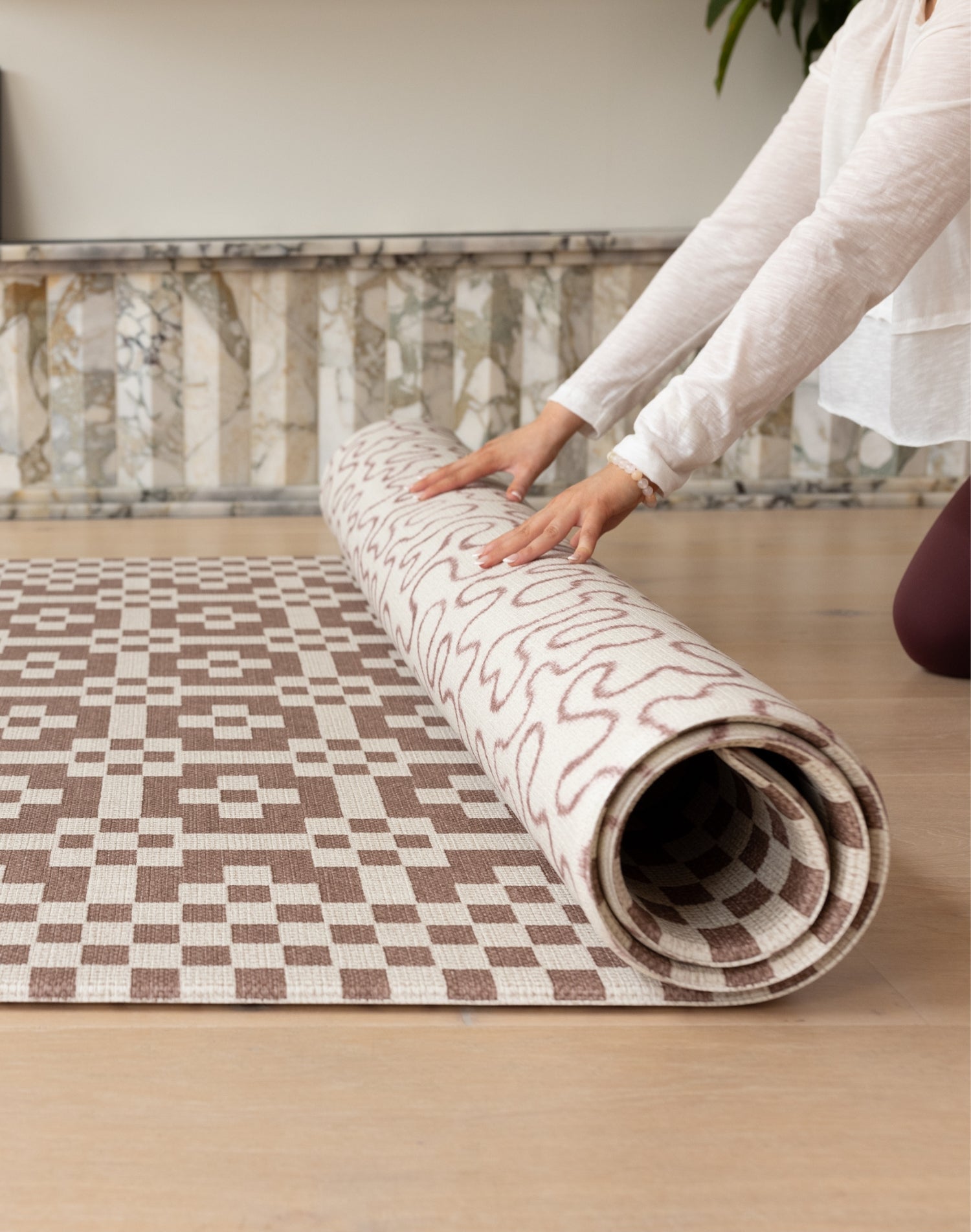 Hands gently roll out a reversible Totter + Tumble play mat for baby. The playmat shows a n earthy motif