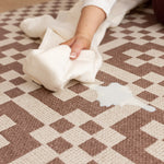 Person cleaning a spill on a patterned play rug with a white cloth.
