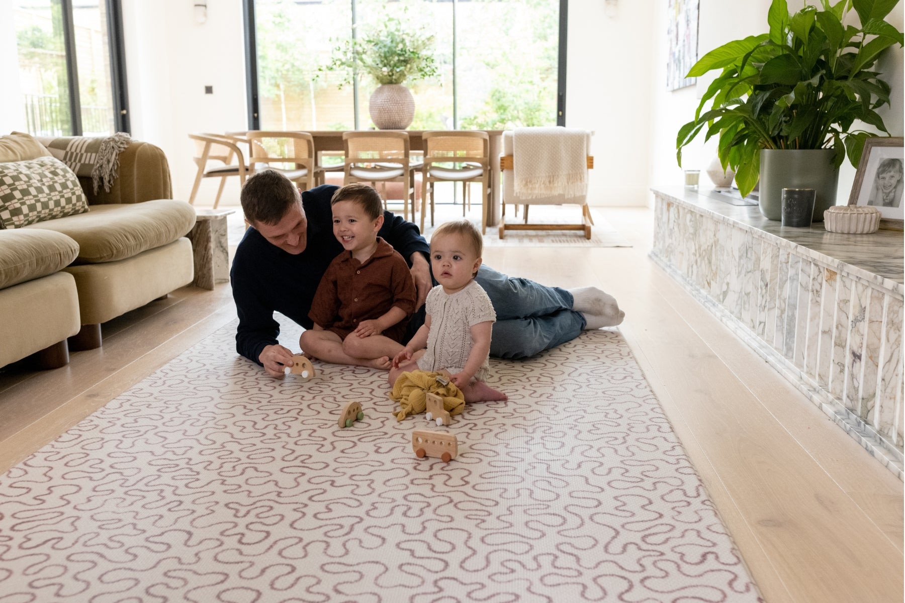 A family sit on a UK designed baby mat in earthy tones. The extra large play mats for toddlers and babies is soft and stylish