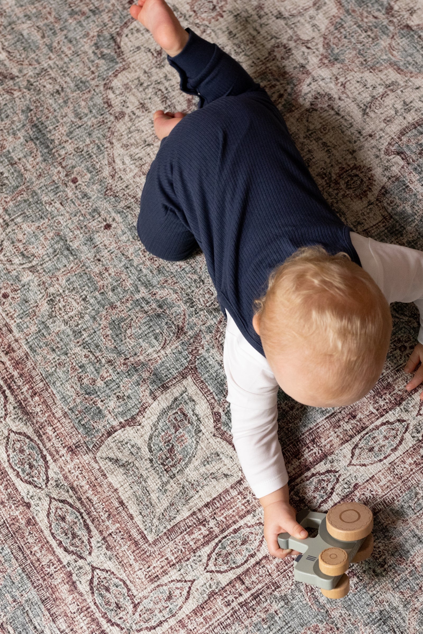 Child playing on a patterned play mat with wooden toys