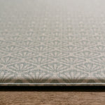 A close-up of a textured thick playmat with a repeating geometric shell pattern in a light blue and grey colour palette