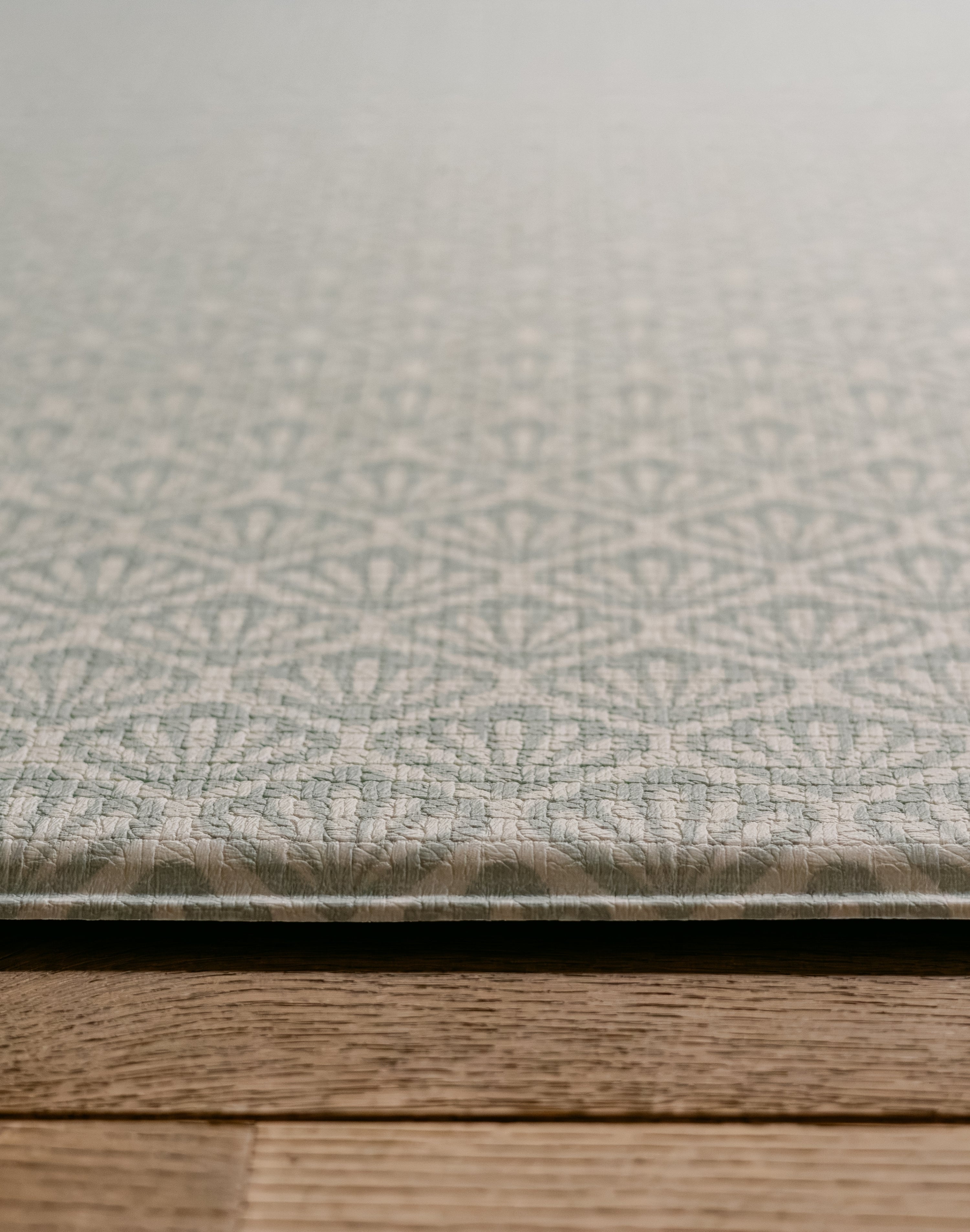 A close-up of a textured thick playmat with a repeating geometric shell pattern in a light blue and grey colour palette