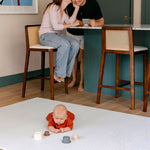 A baby laid on the beachcomber playmat from totter and tumble in the kitchen with family