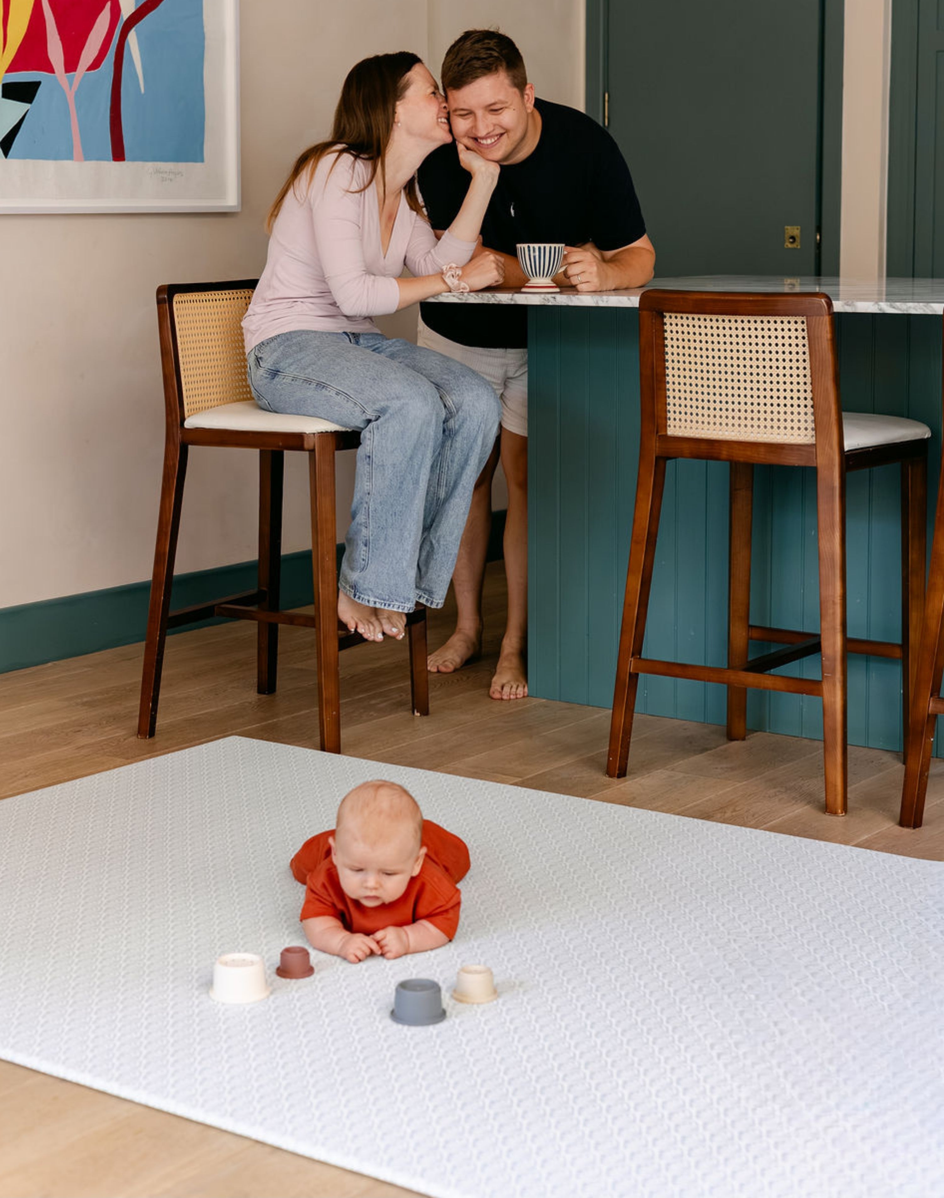 A baby laid on the beachcomber playmat from totter and tumble in the kitchen with family