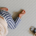 A baby's bare feet and legs wearing blue and white striped pants, crawling on a shell patterned totter and tumble playmat