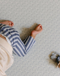 A baby's bare feet and legs wearing blue and white striped pants, crawling on a shell patterned totter and tumble playmat