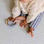 A close up of a baby sat comfortably on a coastal inspired shell design playmat from totter and tumble