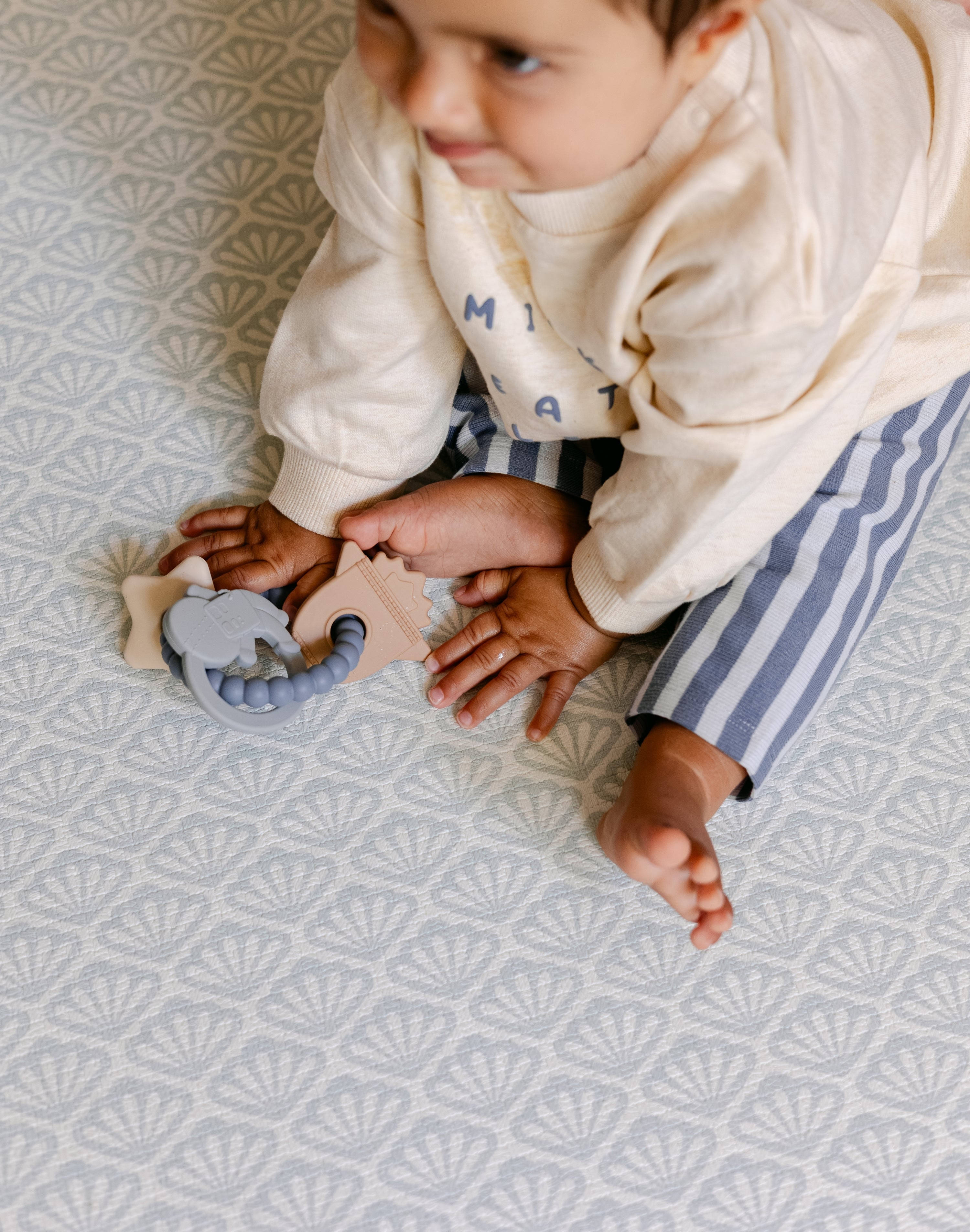 A close up of a baby sat comfortably on a coastal inspired shell design playmat from totter and tumble