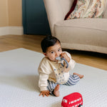 A baby sat on the coastal inspired shell design beachcomber playmat from totter and tumble