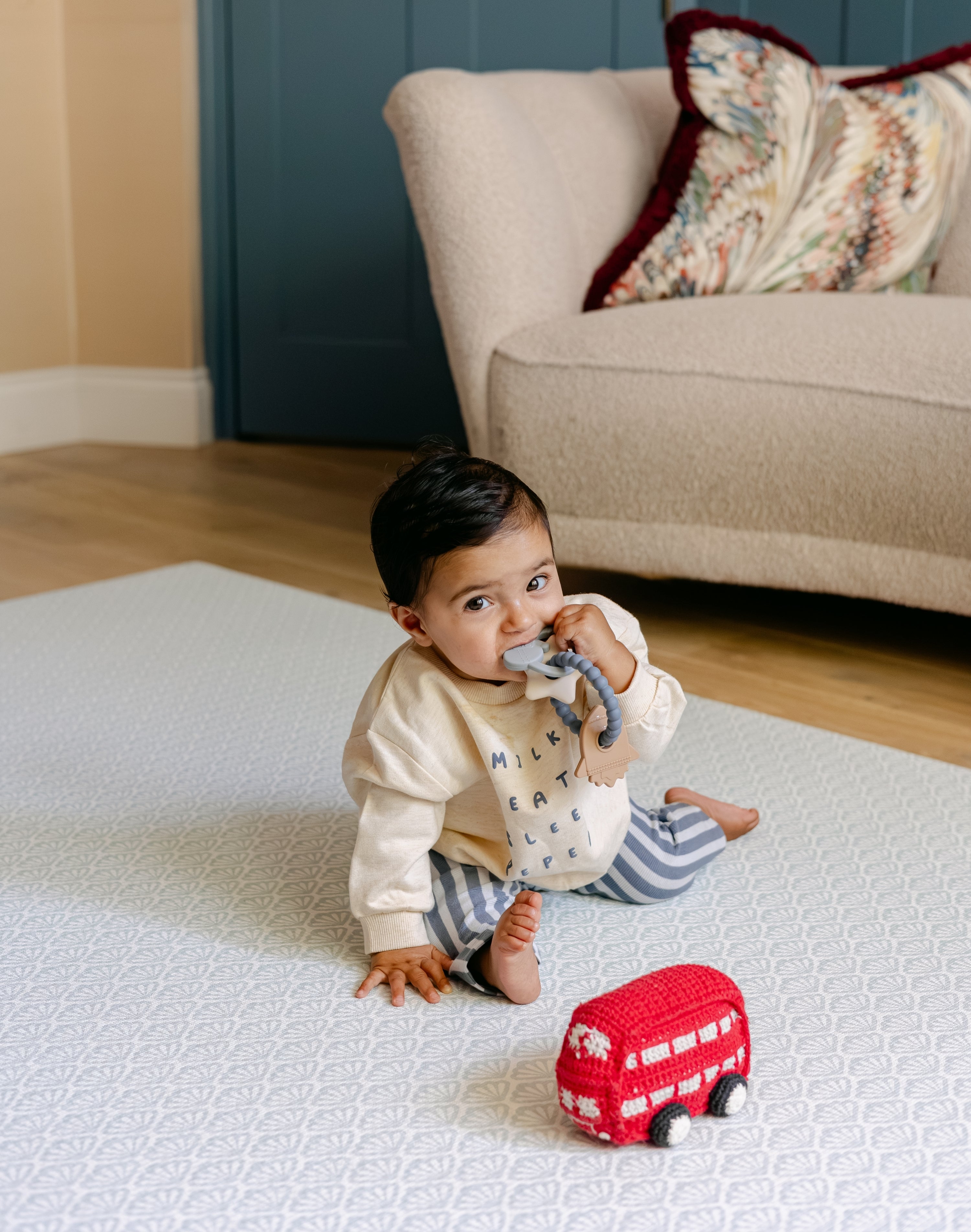 A baby sat on the coastal inspired shell design beachcomber playmat from totter and tumble