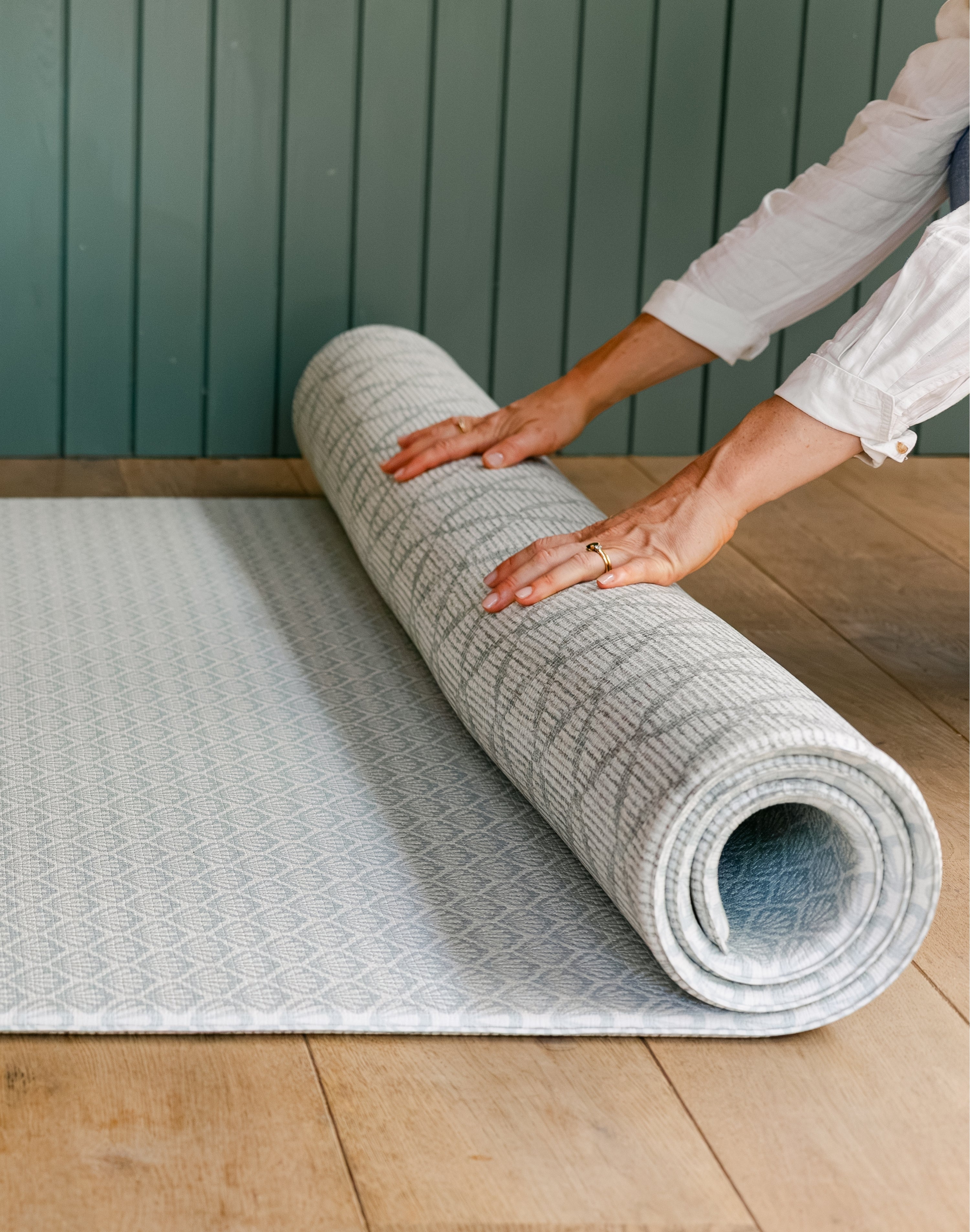 person unrolling the reversible beachcomber shell design playmat from totter and tumble