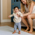 A baby standing up with help from it's mother safe and comfortably on a thick totter and tumble memory foam playmat