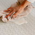 A close-up of a person wiping up split milk easily on a thick memory foam totter and tumble beachcomber playmat