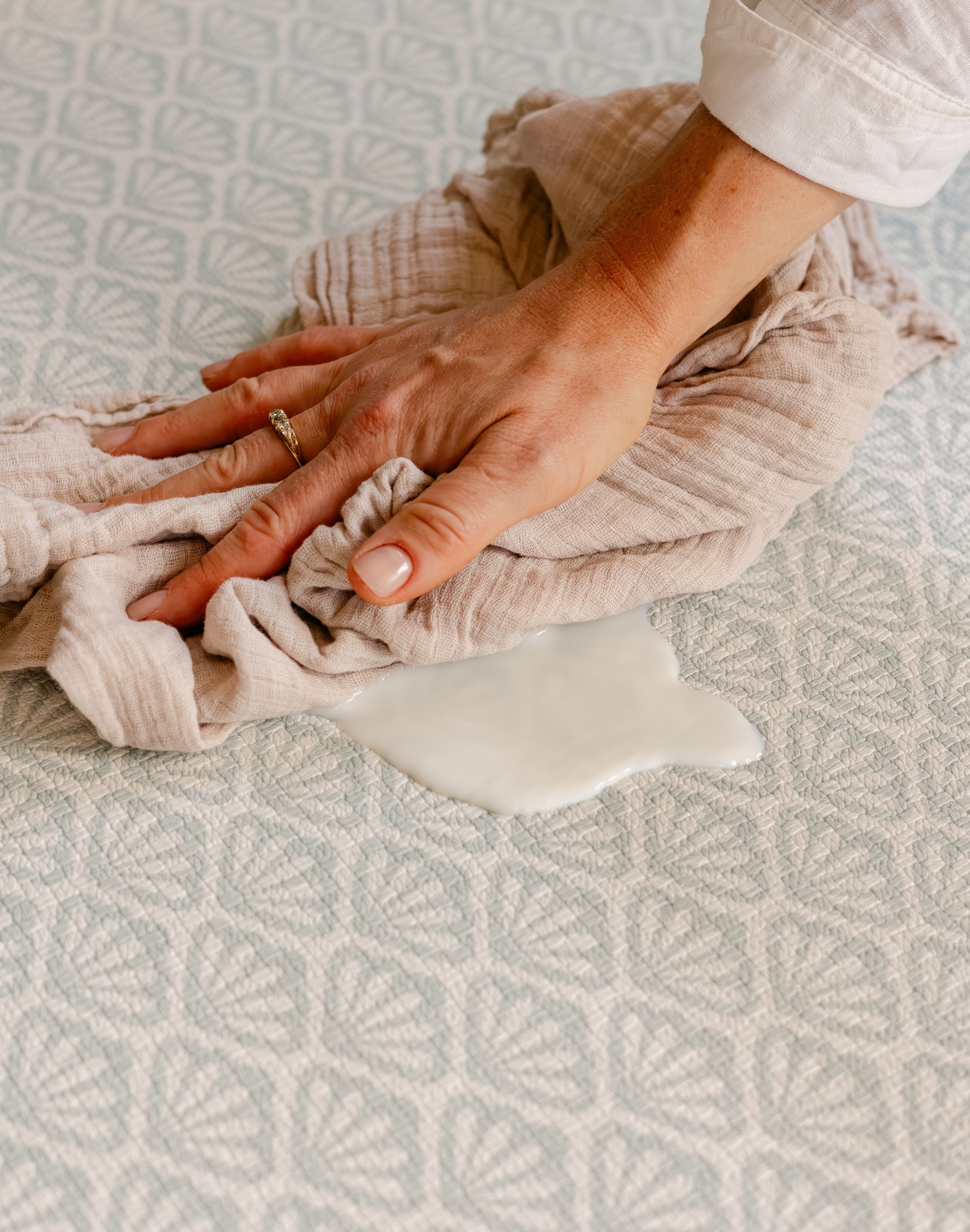 A close-up of a person wiping up split milk easily on a thick memory foam totter and tumble beachcomber playmat