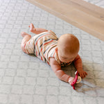 A baby lying on their stomach on a comfy, dafe, non toxic 'the gatherer' playmat from totter and tumble