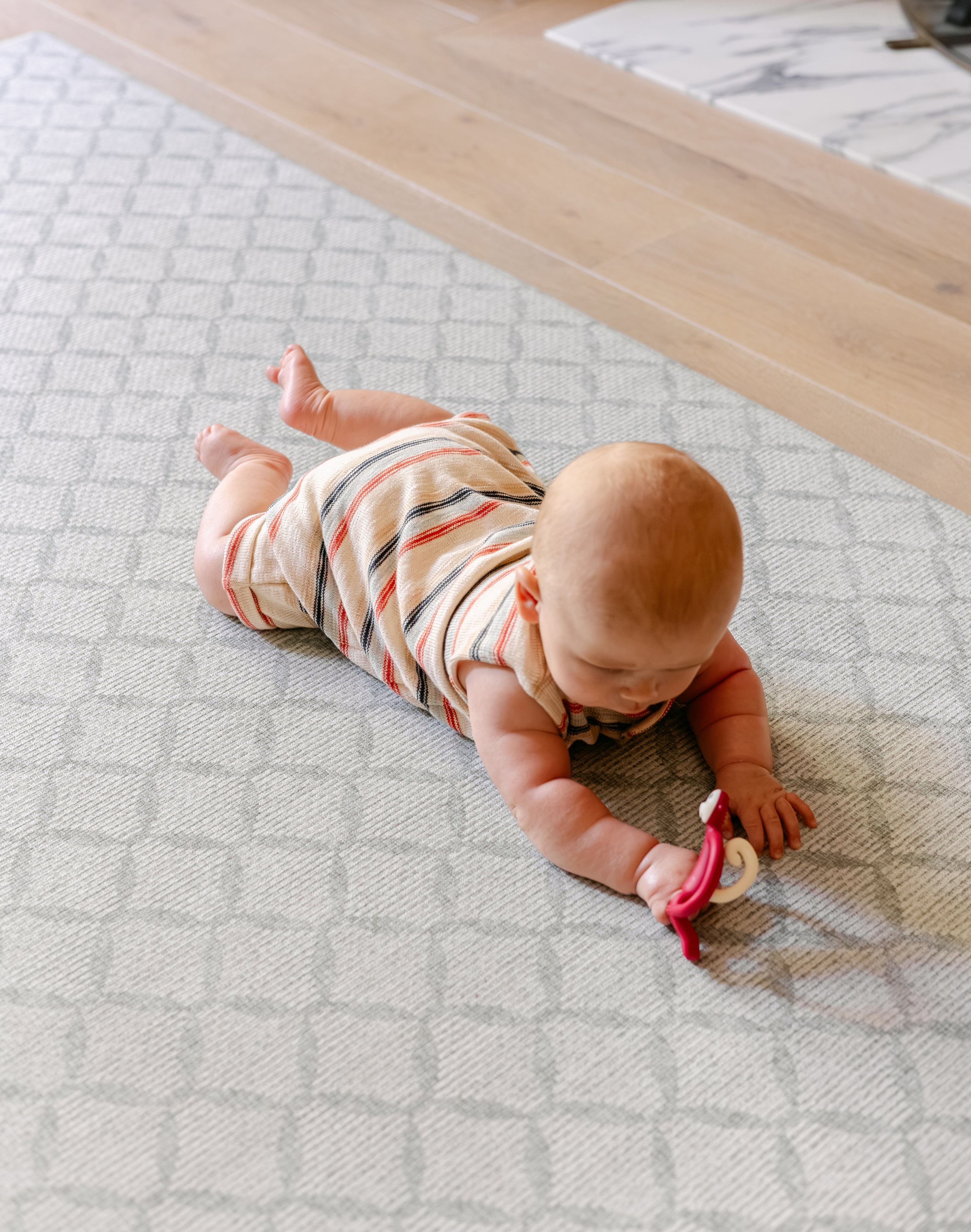 A baby lying on their stomach on a comfy, dafe, non toxic 'the gatherer' playmat from totter and tumble