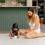 A woman sitting comfortably playing with a baby on a soft thick memory foam playmat from totter and tumble