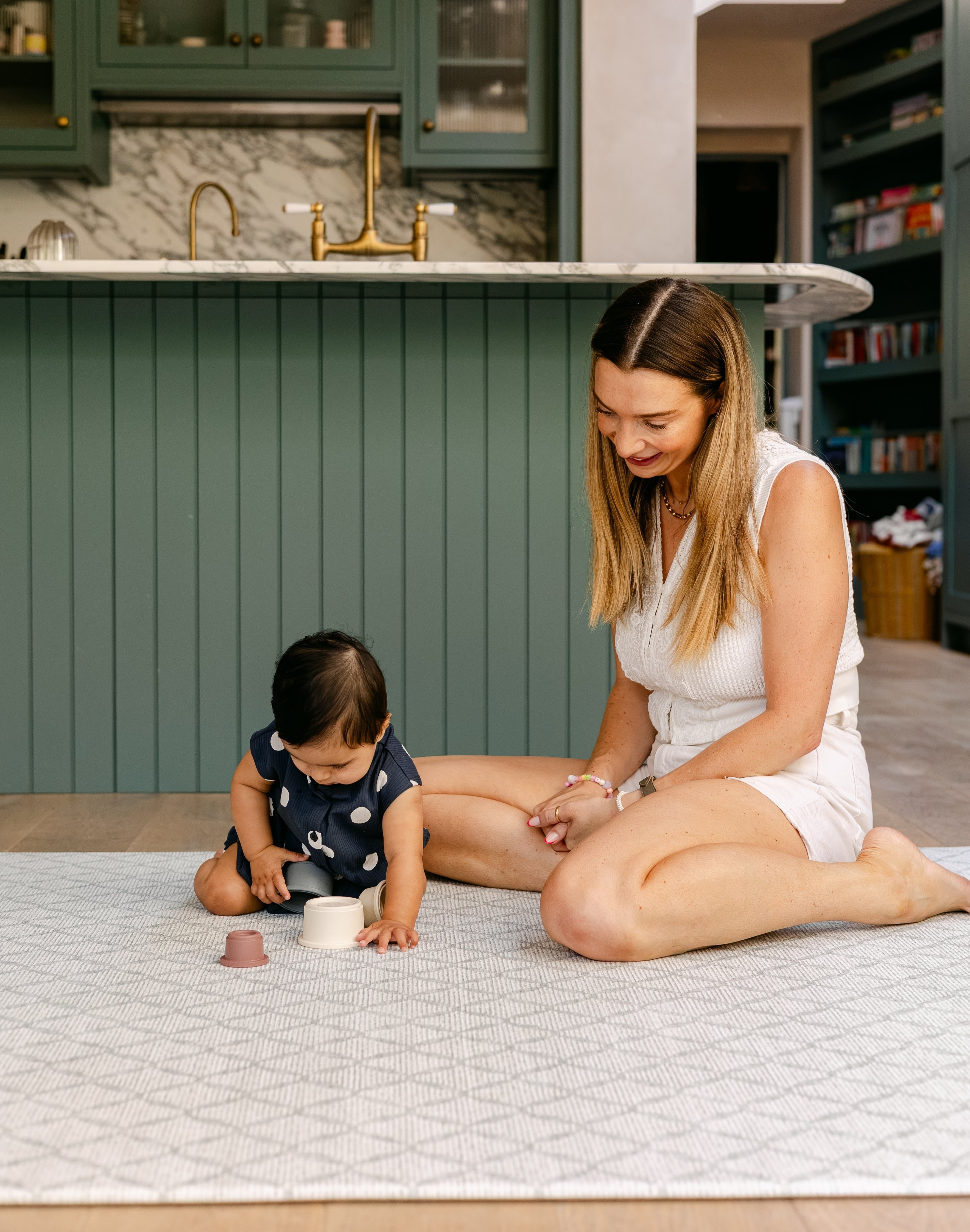 A woman sitting comfortably playing with a baby on a soft thick memory foam playmat from totter and tumble