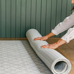 A woman unrolling the gatherer reversible playmat from totter and tumble with geometric pattern