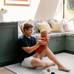 A man sitting comfortably with a baby on a geometric patterned playmat from totter and tumble made out of thick memory foam