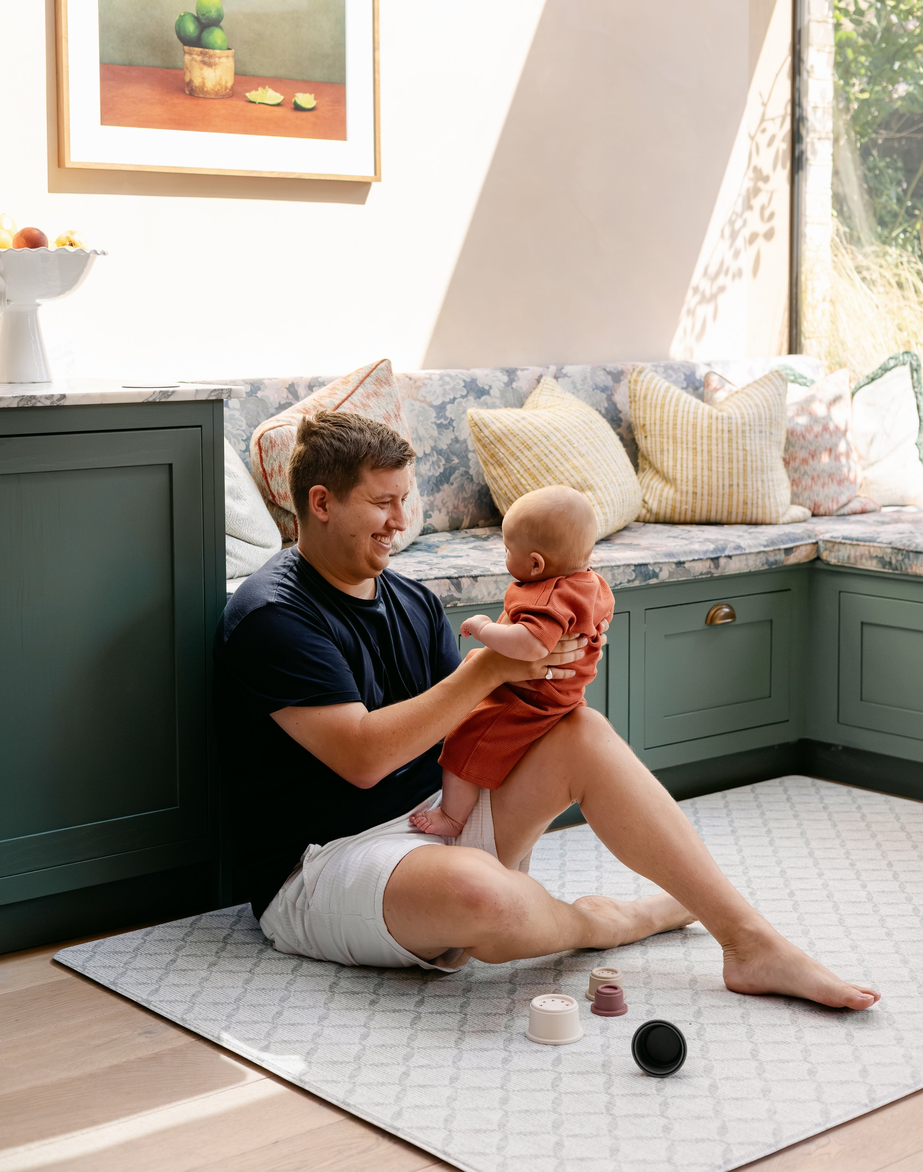 A man sitting comfortably with a baby on a geometric patterned playmat from totter and tumble made out of thick memory foam