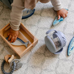 A baby playing with toys on a geometric patterned soft wipeable playmat from totter and tumble