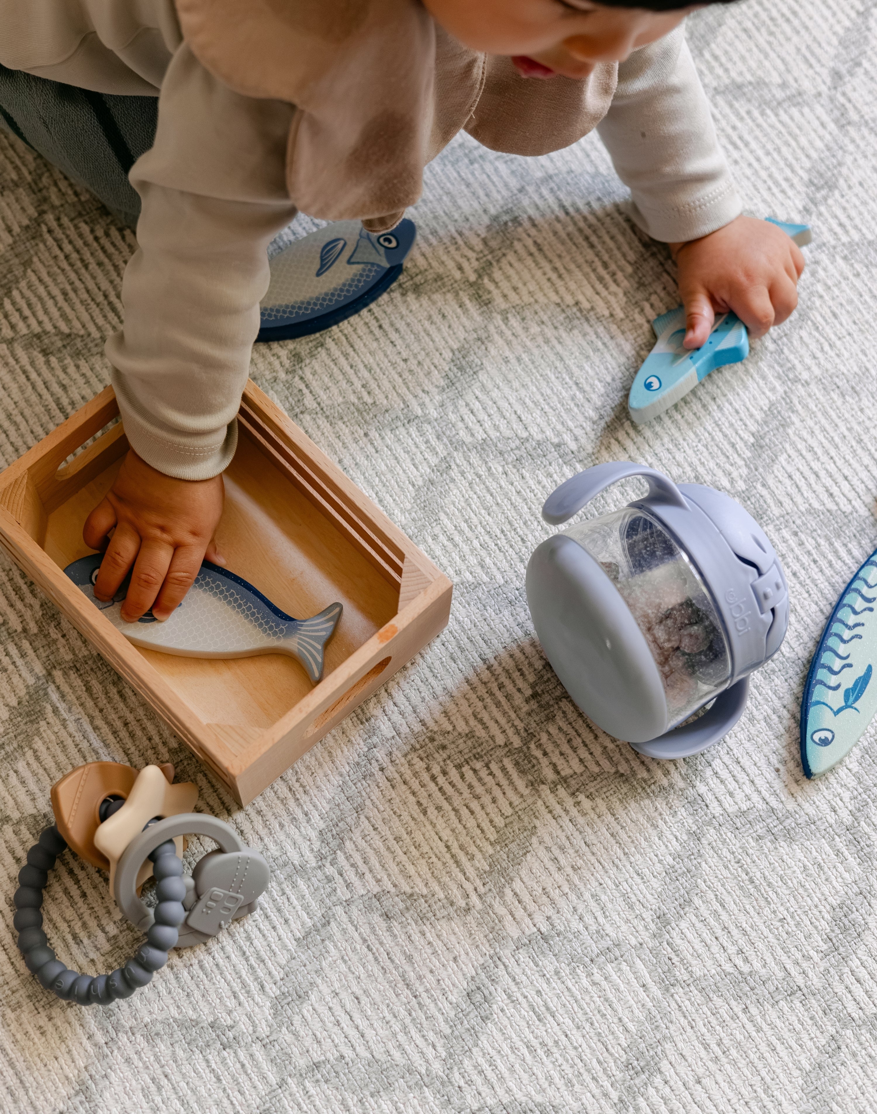A baby playing with toys on a geometric patterned soft wipeable playmat from totter and tumble