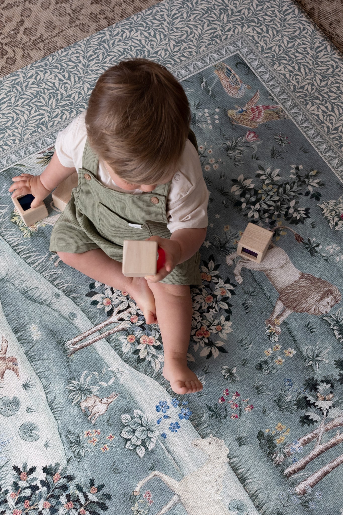 Child playing on a patterned rug in a room with wooden floor and furniture.