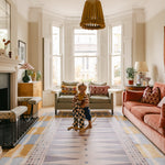 Child on rocking horse in bright living room with colourful interiors and The Roller memory foam reversible Playmat by Totter + Tumble, the biggest one piece playmat on the market