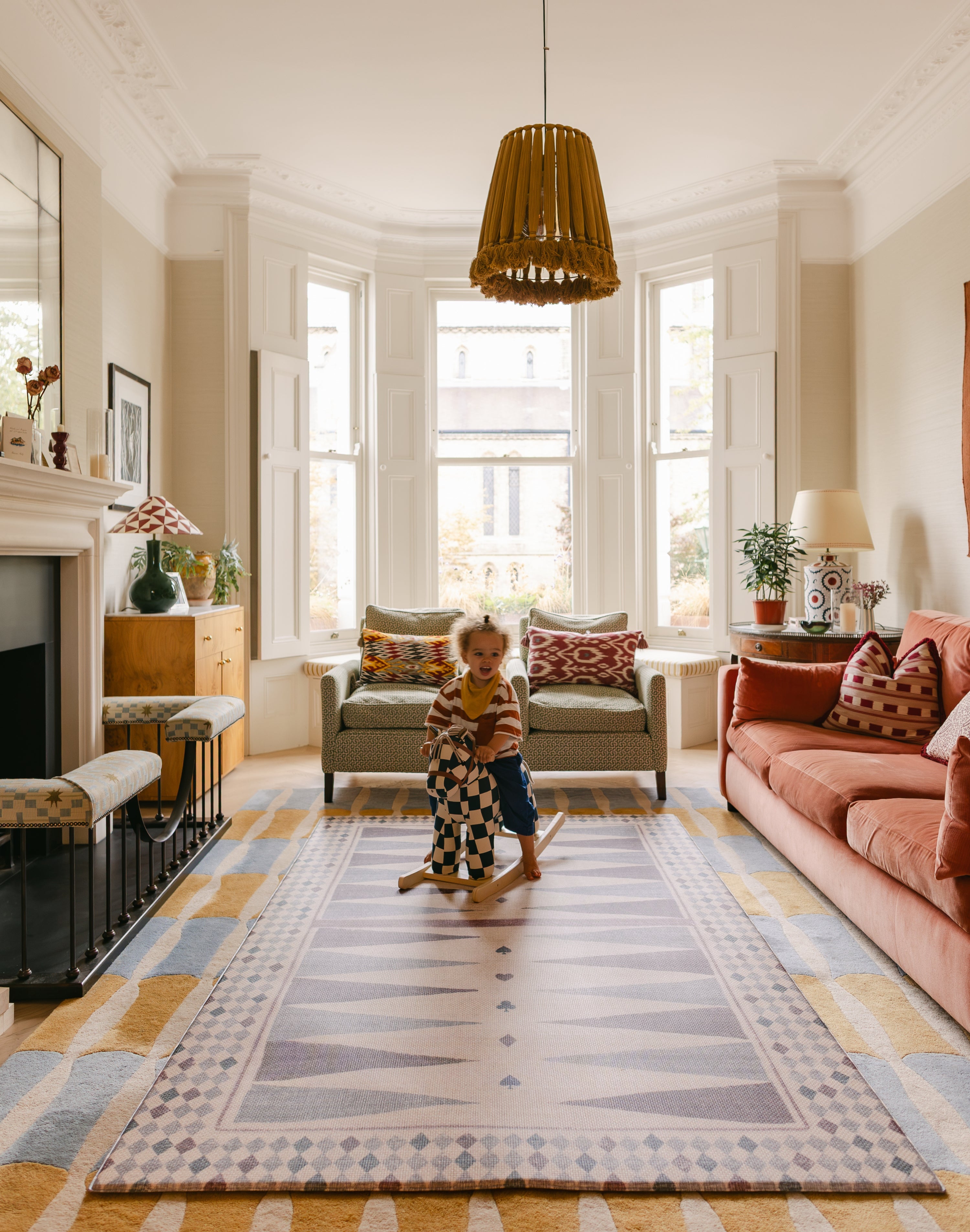Child on rocking horse in bright living room with colourful interiors and The Roller memory foam reversible Playmat by Totter + Tumble, the biggest one piece playmat on the market