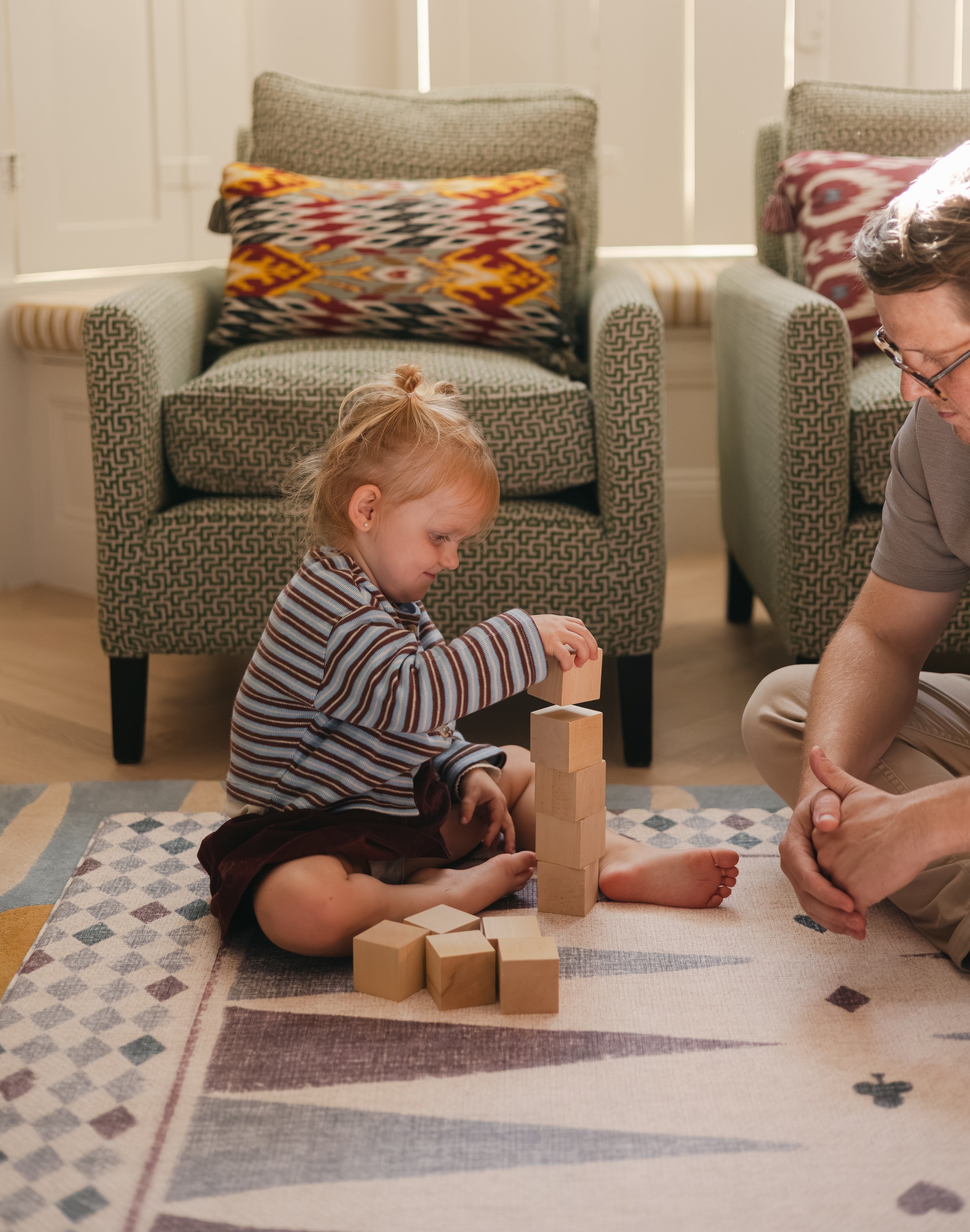 Child stacking blocks on The Roller Playmat by Totter + Tumble, the biggest one piece playmat on the market, watched by a man