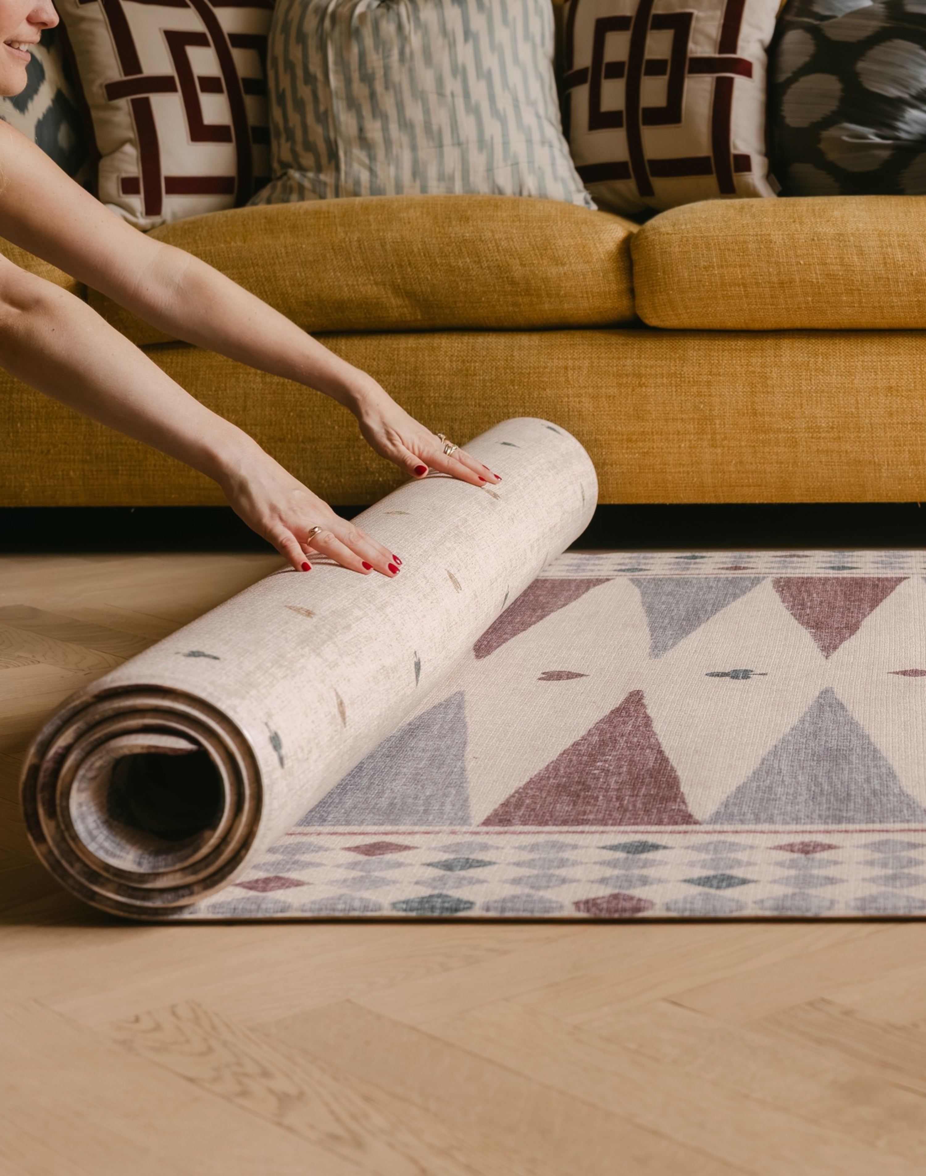 Hands rolling The Roller Playmat by Totter + Tumble, the biggest one piece playmat on the market, next to a bright yellow sofa