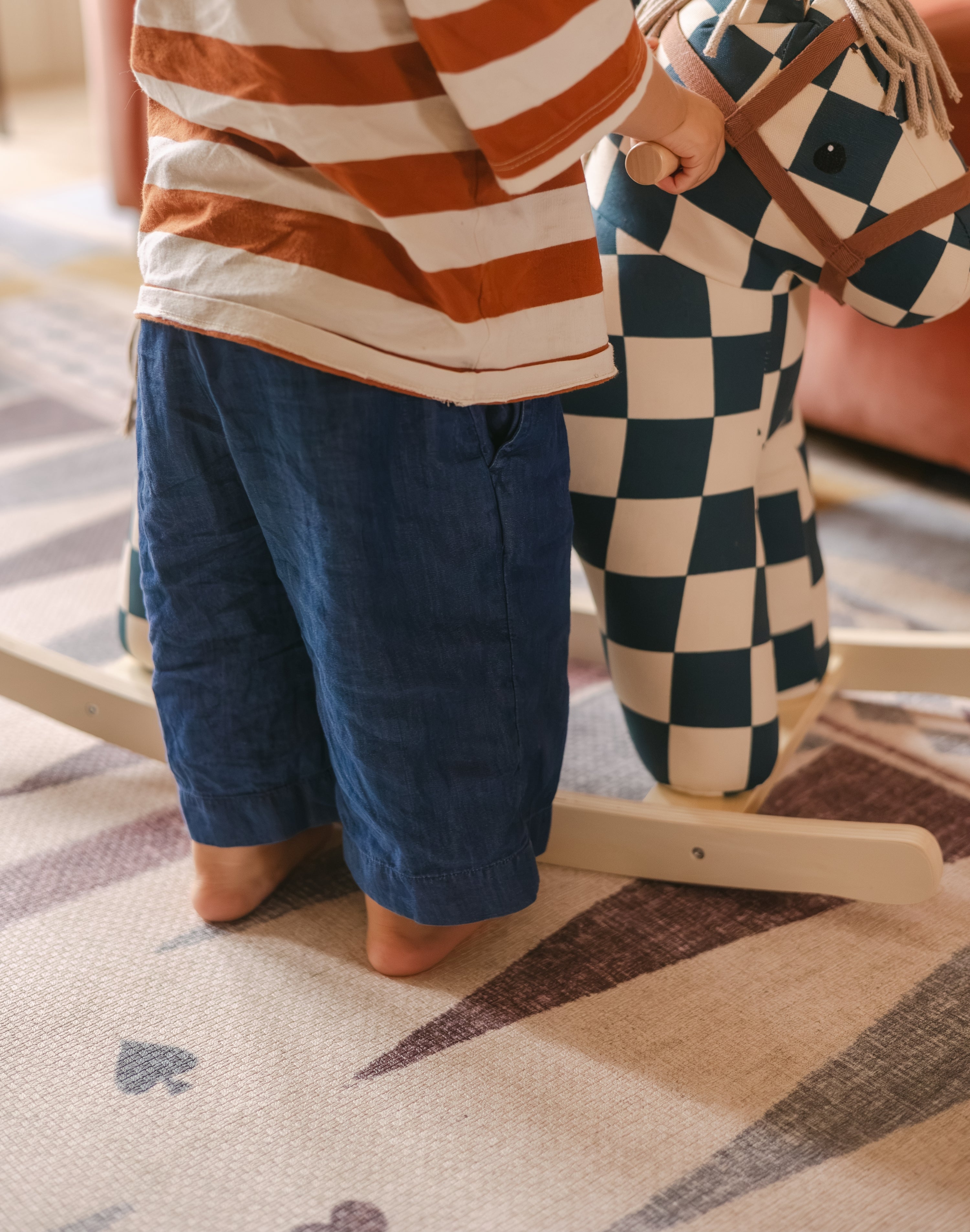 Toddler toes on The Roller Playmat by Totter + Tumble, the biggest one piece playmat on the market, next to a colourful rocking horse