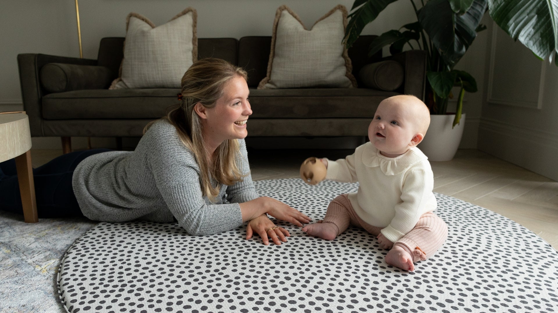Mum and baby lie and sit on a spotty round playmat