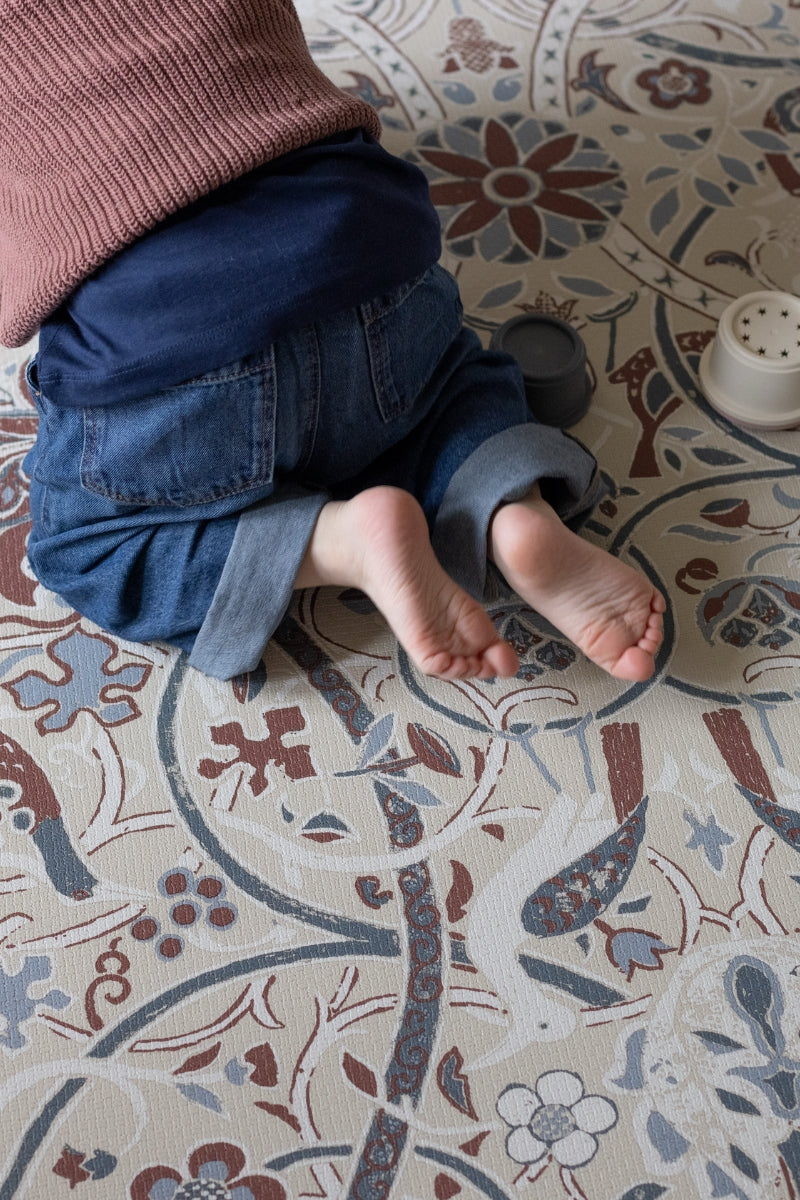 Child on a Morris & Co patterned playmat