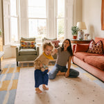 Mum and toddler playing on The Wildcard Totter + Tumble reversible wipeable memory foam playmat in a colourful living space