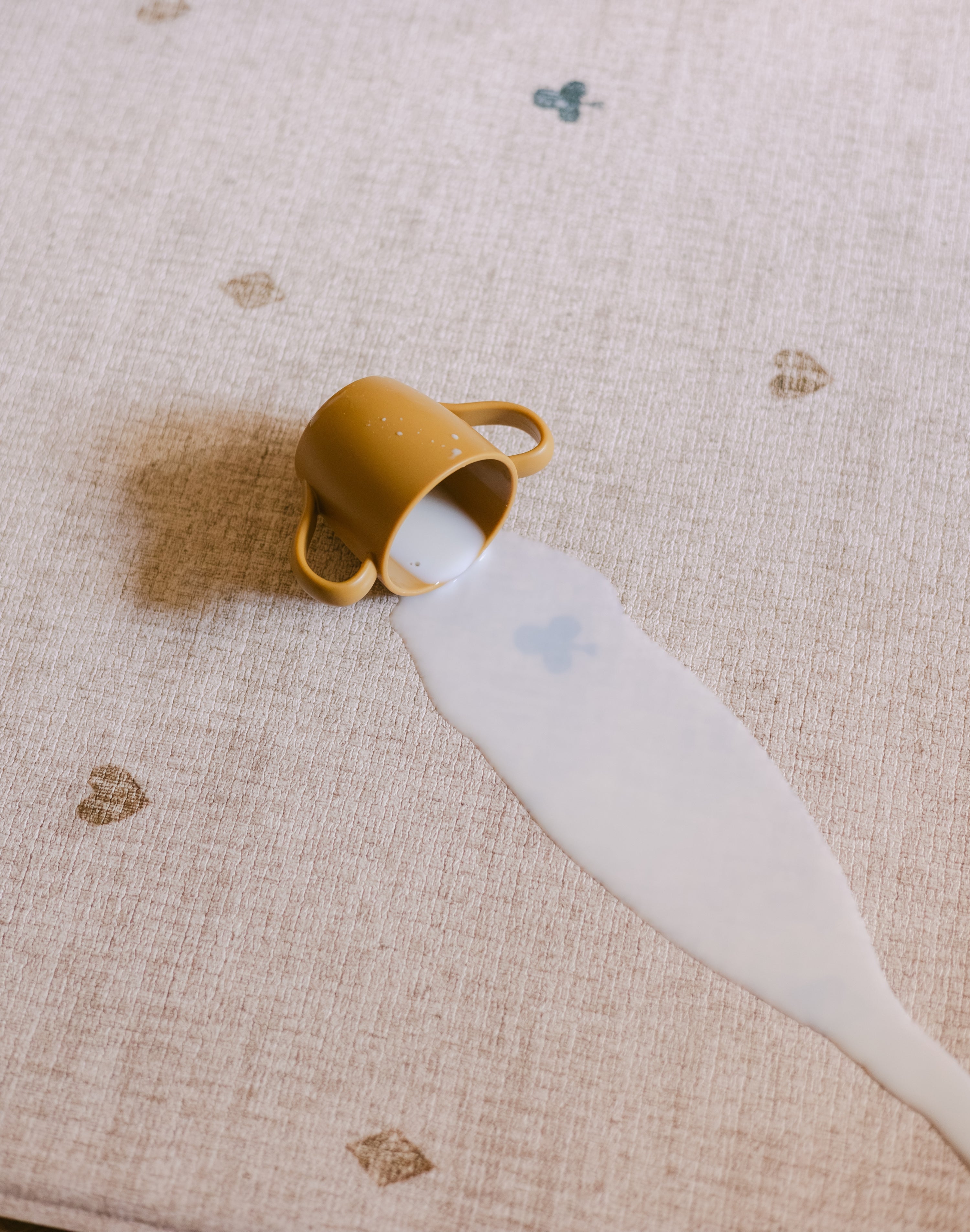 A baby cup and milk spilled on The Wildcard Totter + Tumble reversible wipeable memory foam playmat
